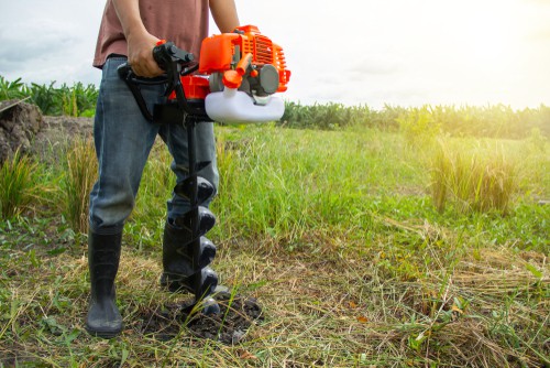 Garden centre using petrol auger to dog holes for planting